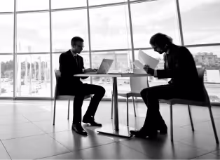 Two colleagues working at a table beside a floor-to-ceiling office window