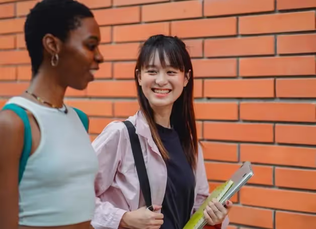 Two students talking outside a brick campus building, one carrying course books