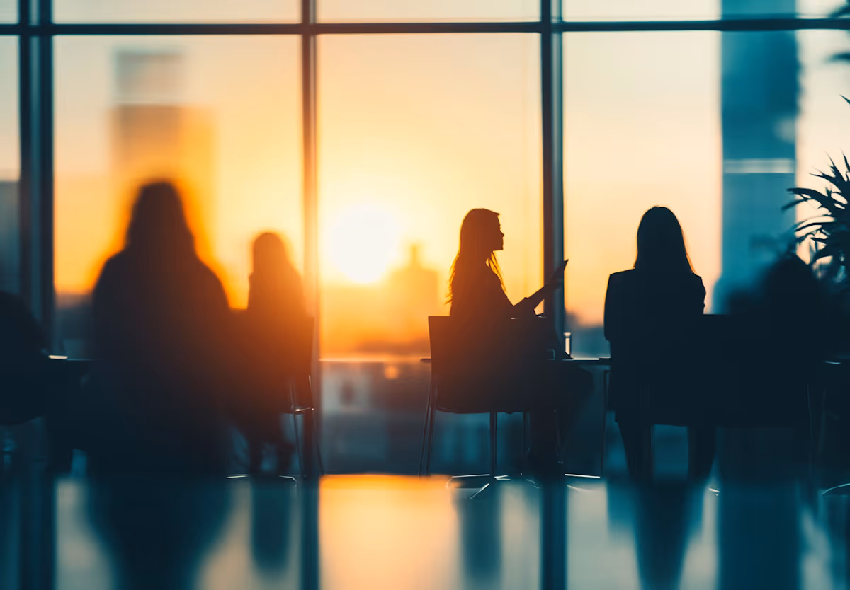 Silhouetted professionals in a meeting room with floor-to-ceiling windows at sunset, representing a collaborative engineering engagement between distributed teams.